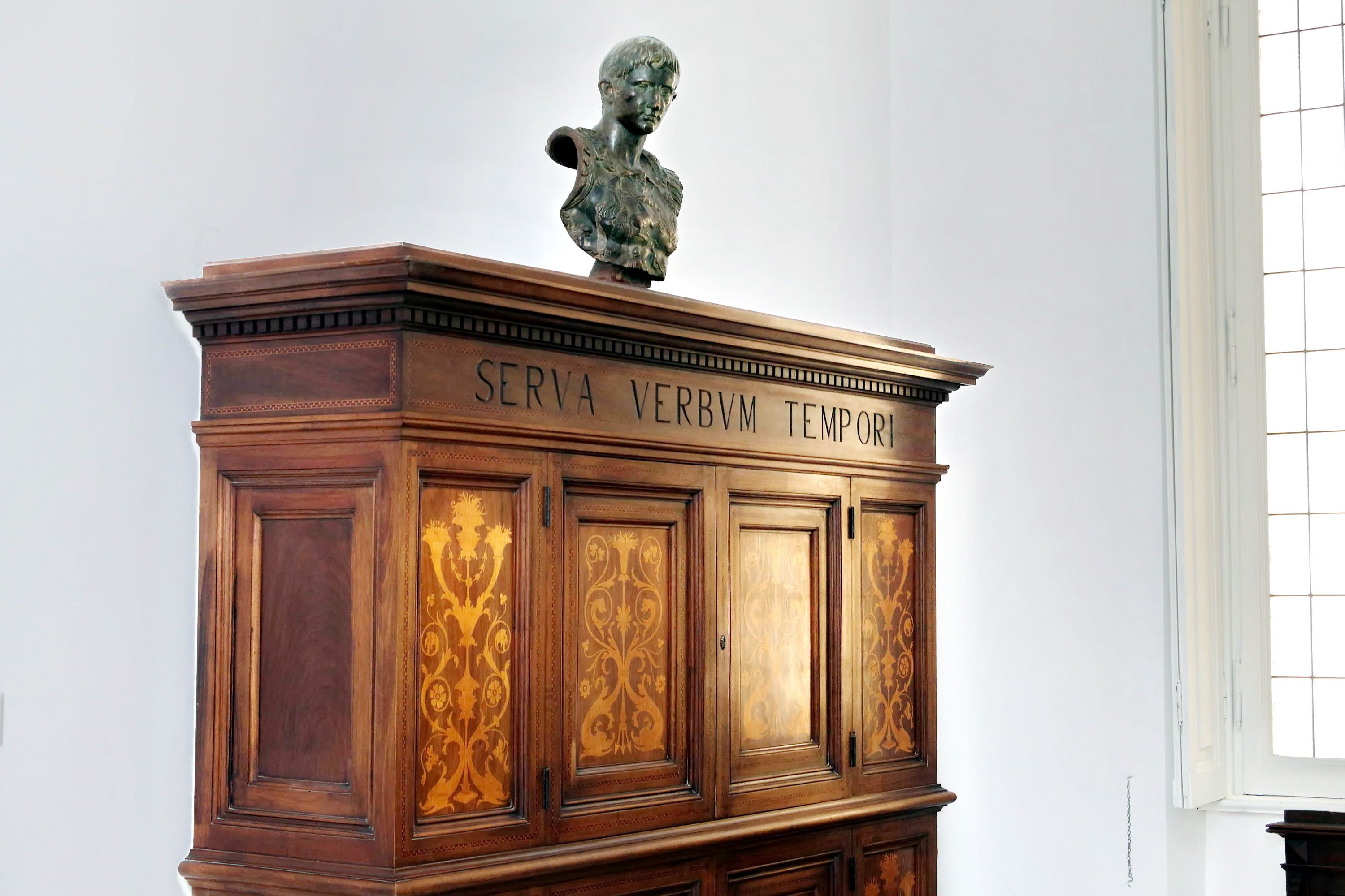 Un gabinete de madera con un busto encima y la inscripción “SERVA VERBVM TEMPOR”.