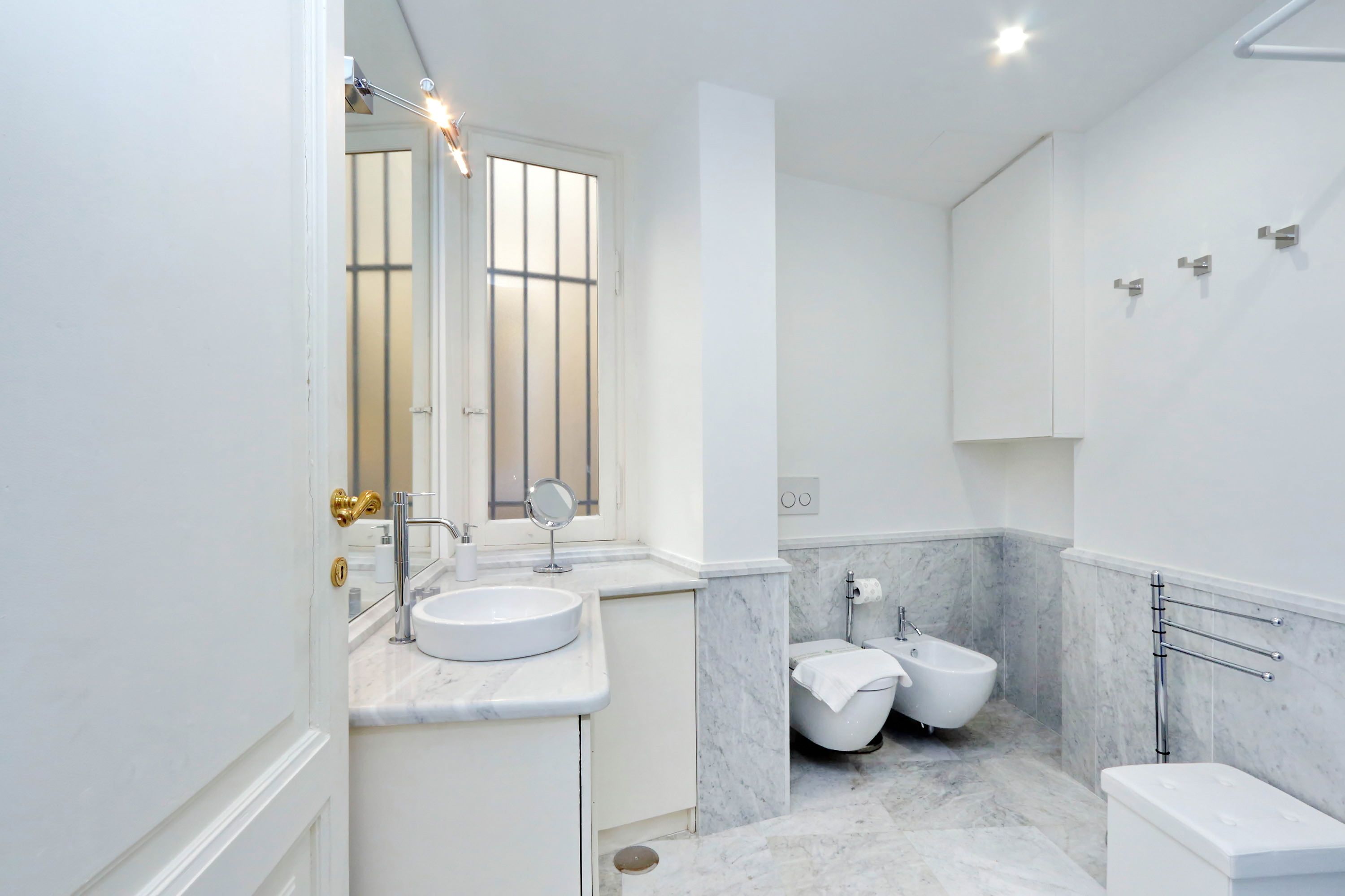 A modern bathroom with a white sink, a mirror, a toilet, and a bidet.