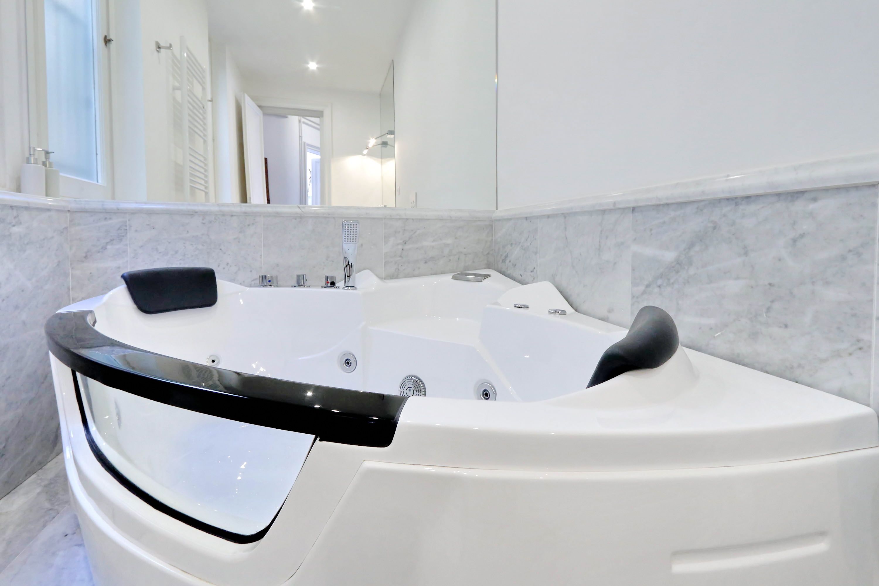 Un baño moderno con una bañera blanca grande, una pared de mármol y un espejo que refleja la habitación.