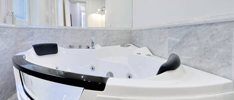 Un baño moderno con una bañera blanca grande, una pared de mármol y un espejo que refleja la habitación.