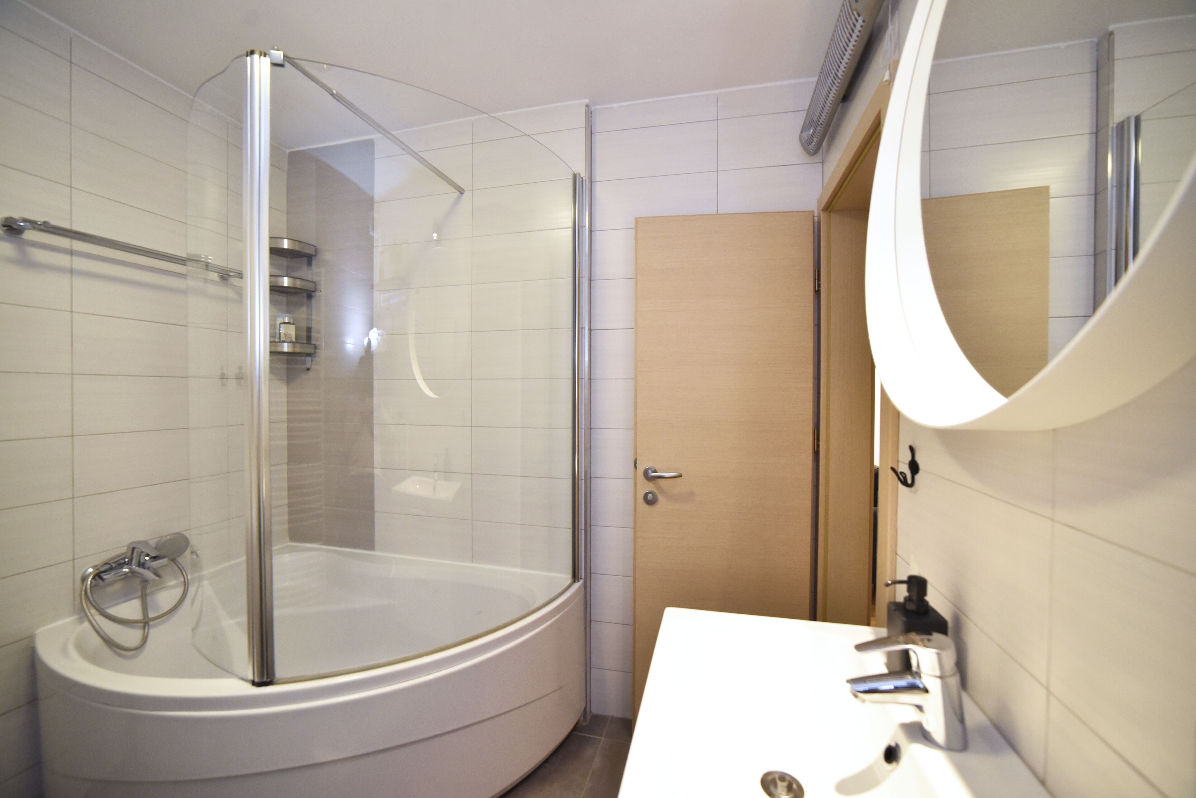 A modern bathroom with a glass-enclosed shower, a white sink, and a wooden door.