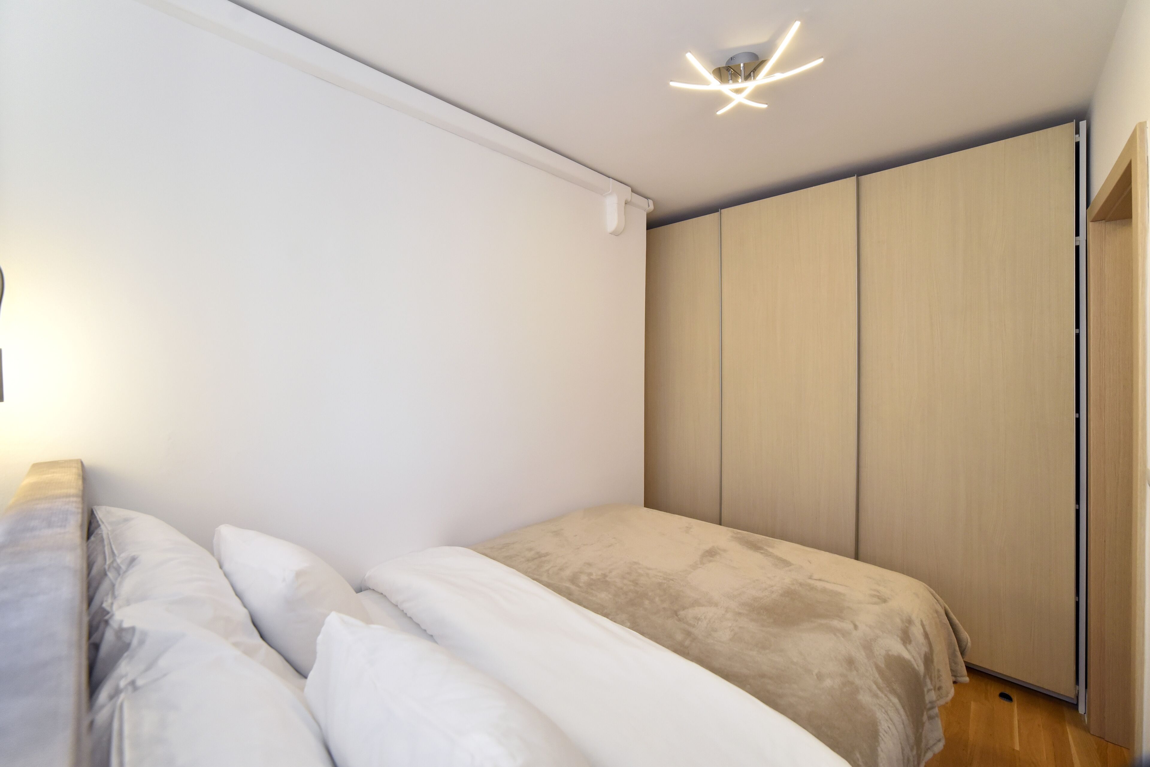 A modern bedroom with a bed, a wardrobe, and a ceiling light fixture.