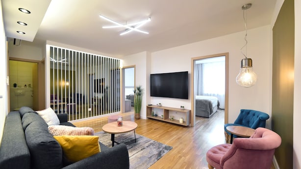 A modern living room with a sofa, a pink armchair, a TV, and a wooden floor. - Apartment First Choice Ilica (Zagreb)