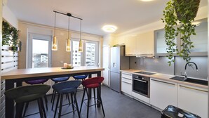 A modern kitchen with a central island, bar stools, stainless steel appliances, and hanging plants. - Apartment First Choice Ilica (Zagreb)