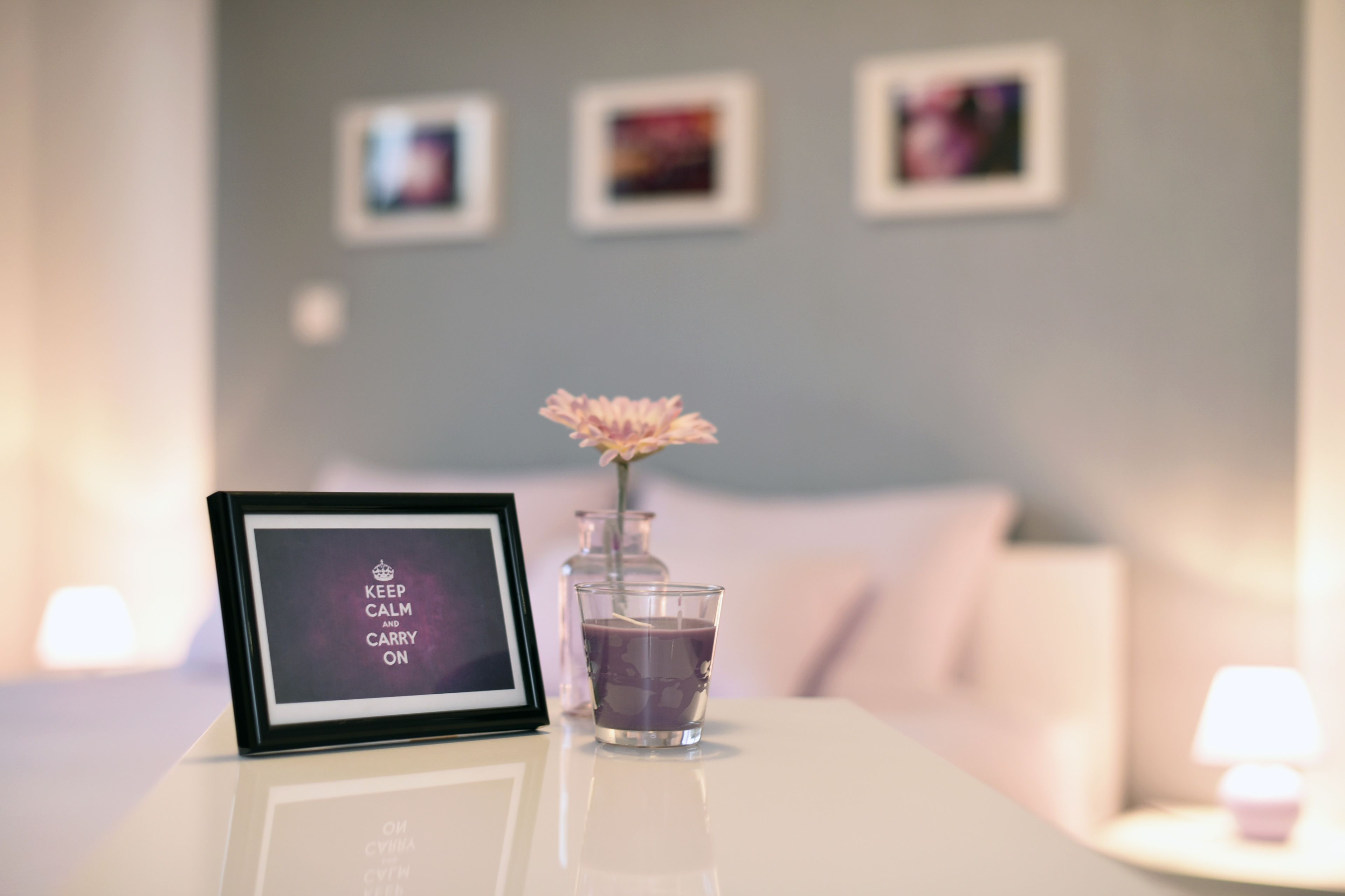 A framed sign with text, a glass candle holder with a flower, and a candle on a white table in a hotel room.
