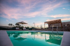 Ein Swimmingpool mit Liegestühlen und Sonnenschirmen, umgeben von Steinmauern und einer Pergola.