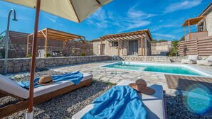 A pool area with lounge chairs, a pergola, and a stone building. - Roggaki Ionian Villas (Aktio-Vonitsa)