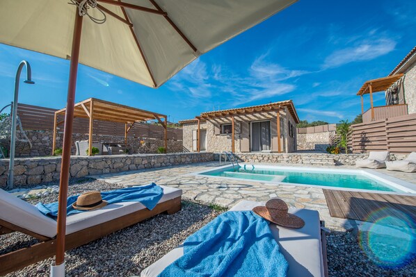 Ein Poolbereich mit Liegestühlen, einer Pergola und einem Steinhaus.