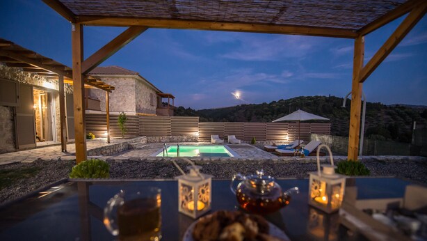 An outdoor pool area with a pergola, a table with drinks and snacks, and a view of the surrounding landscape. - Roggaki Ionian Villas (Aktio-Vonitsa)