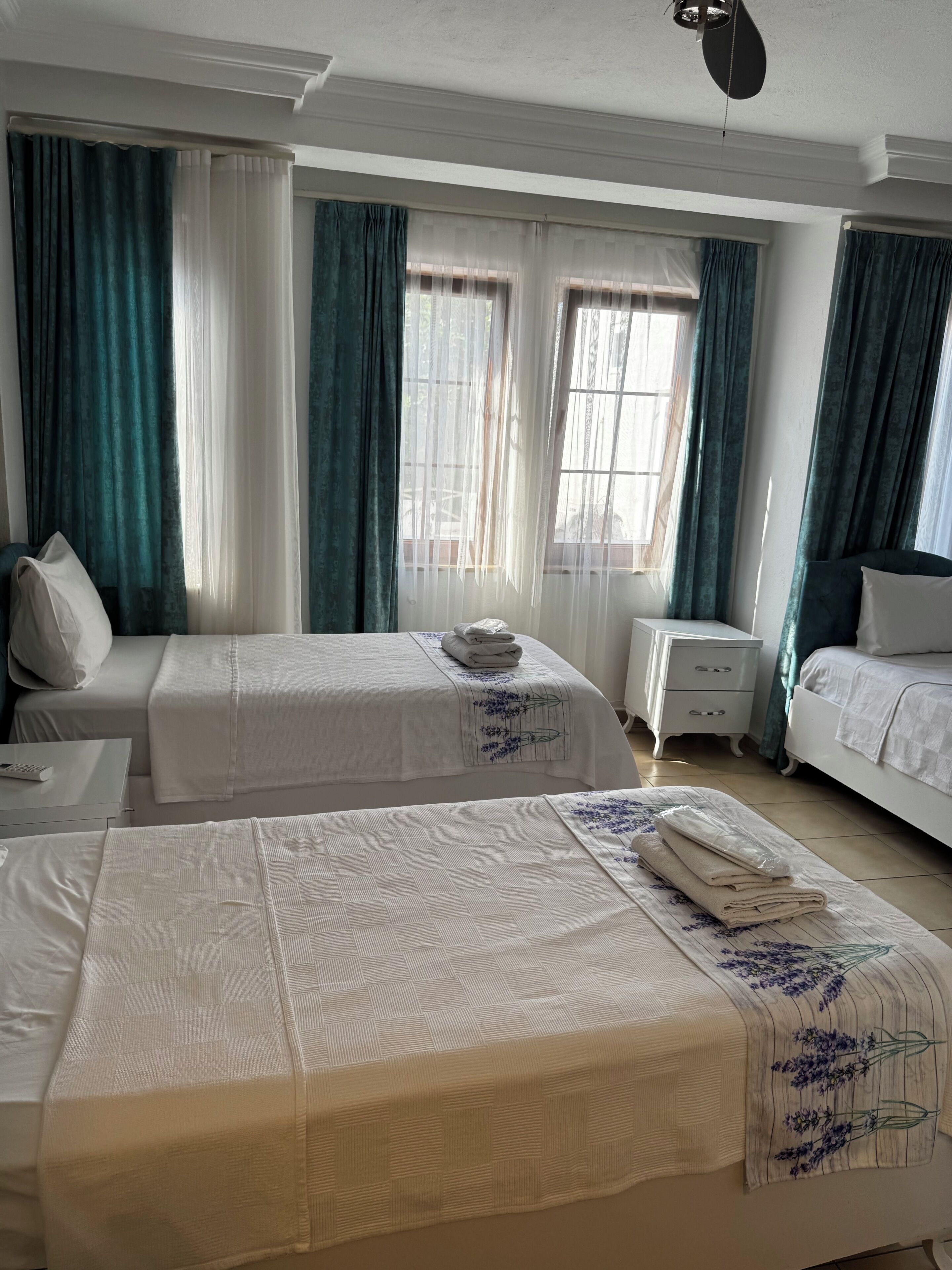 A hotel room with two beds, a nightstand, a dresser, and a window with curtains.
