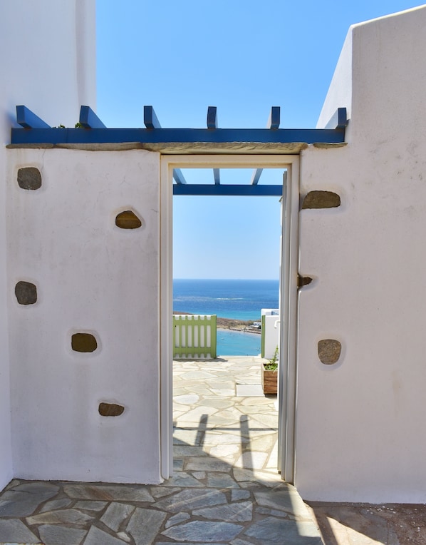 An open doorway leading to a stone patio with a view of the sea.
