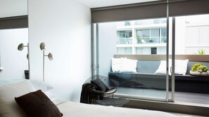 A modern hotel room with a large window, a bed, a chair, and a floor lamp.