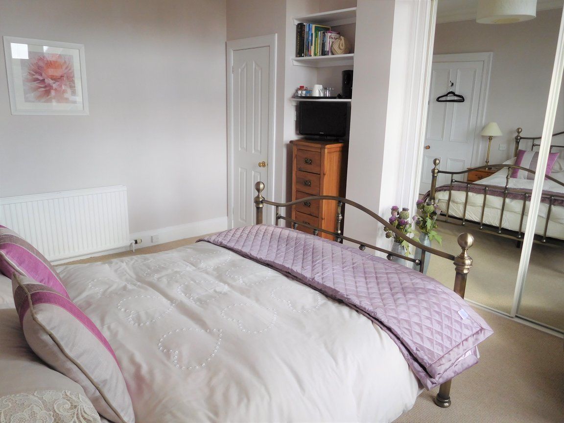 A bedroom with a bed, a dresser, a television, and a door leading to another room.