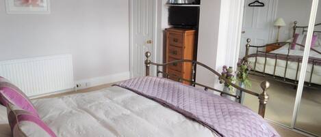 A bedroom with a bed, a dresser, a television, and a door leading to another room.