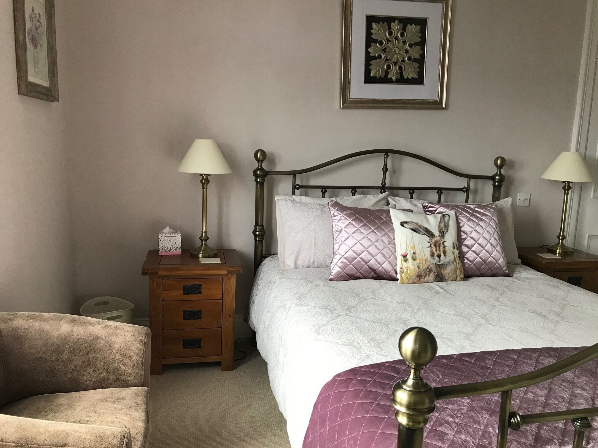 A bedroom with a bed, two bedside tables with lamps, a chair, and a wall-mounted picture frame.