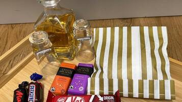 A wooden tray with a glass bottle, two shot glasses, a striped cloth, and various candy bars including KitKat and Snickers.