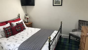 A bedroom with a bed, a TV, a framed picture, and a chair.