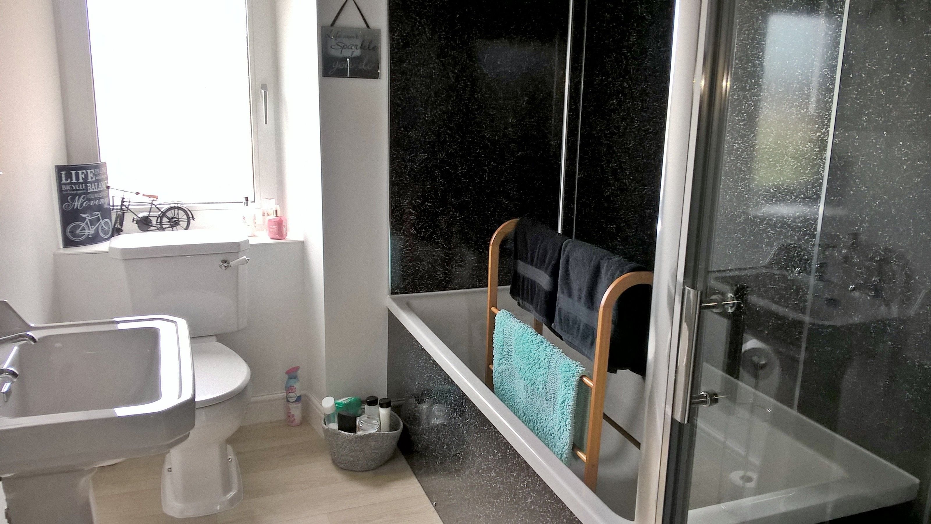 A bathroom with a toilet, sink, and shower. There is a window with a bicycle sign, a towel rack with towels, and a small trash bin.