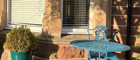A house with a stone facade, a window with blinds, a potted plant, and a blue metal table and chair set.