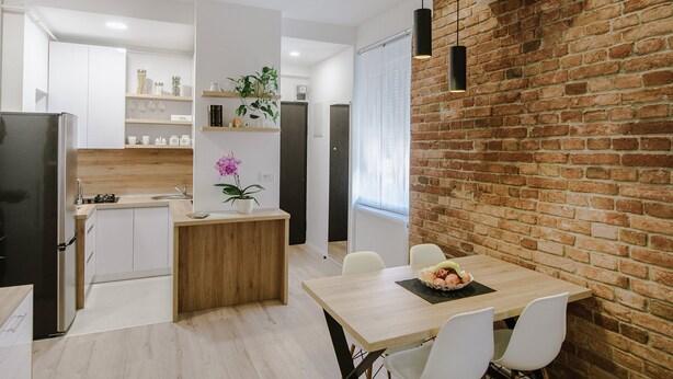 Una cocina moderna con armarios blancos, una isla de madera y una pared decorativa de ladrillo.