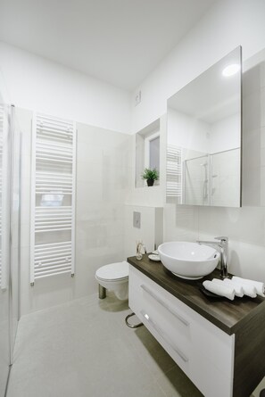 A modern bathroom with a white toilet, a large mirror, a white sink, and a shower area. - Apartment British Square (Zagreb)