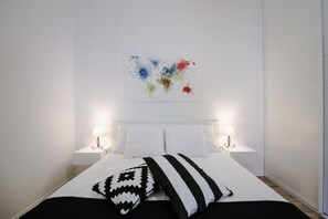 A neatly made bed with white linens, two bedside lamps, and a colorful abstract painting on the wall. - Apartment British Square (Zagreb)