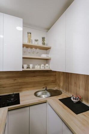 A modern kitchen with white cabinets, wooden shelves, a stainless steel sink, and a black countertop. - Apartment British Square (Zagreb)
