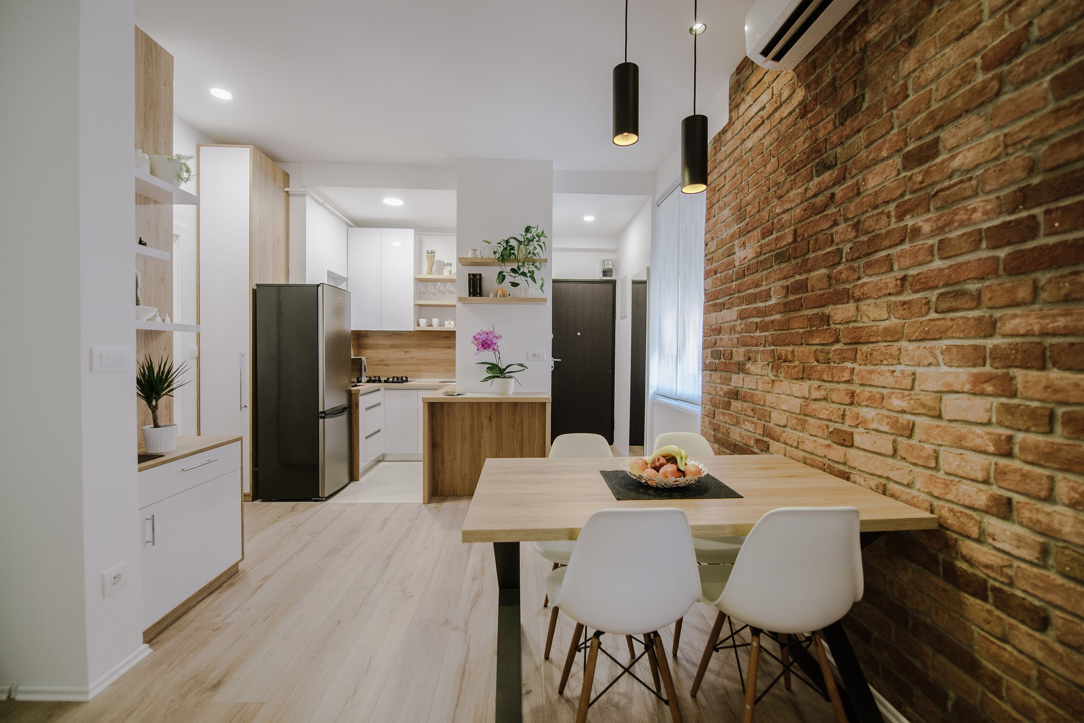 A modern kitchen with white cabinetry, a wooden dining table, and a brick accent wall.