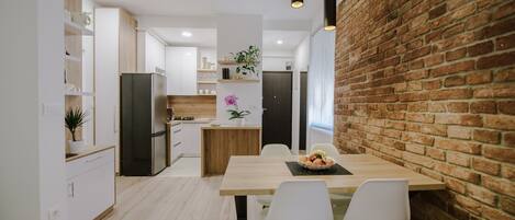 A modern kitchen with white cabinetry, a wooden dining table, and a brick accent wall.