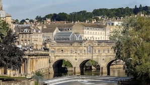 Eine historische Steinbrücke mit drei Bögen über einem Fluss, umgeben von Gebäuden und Bäumen.