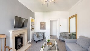 Ein Wohnzimmer mit Kamin, Fernseher, zwei Sesseln, einer Couch und einem Couchtisch.
