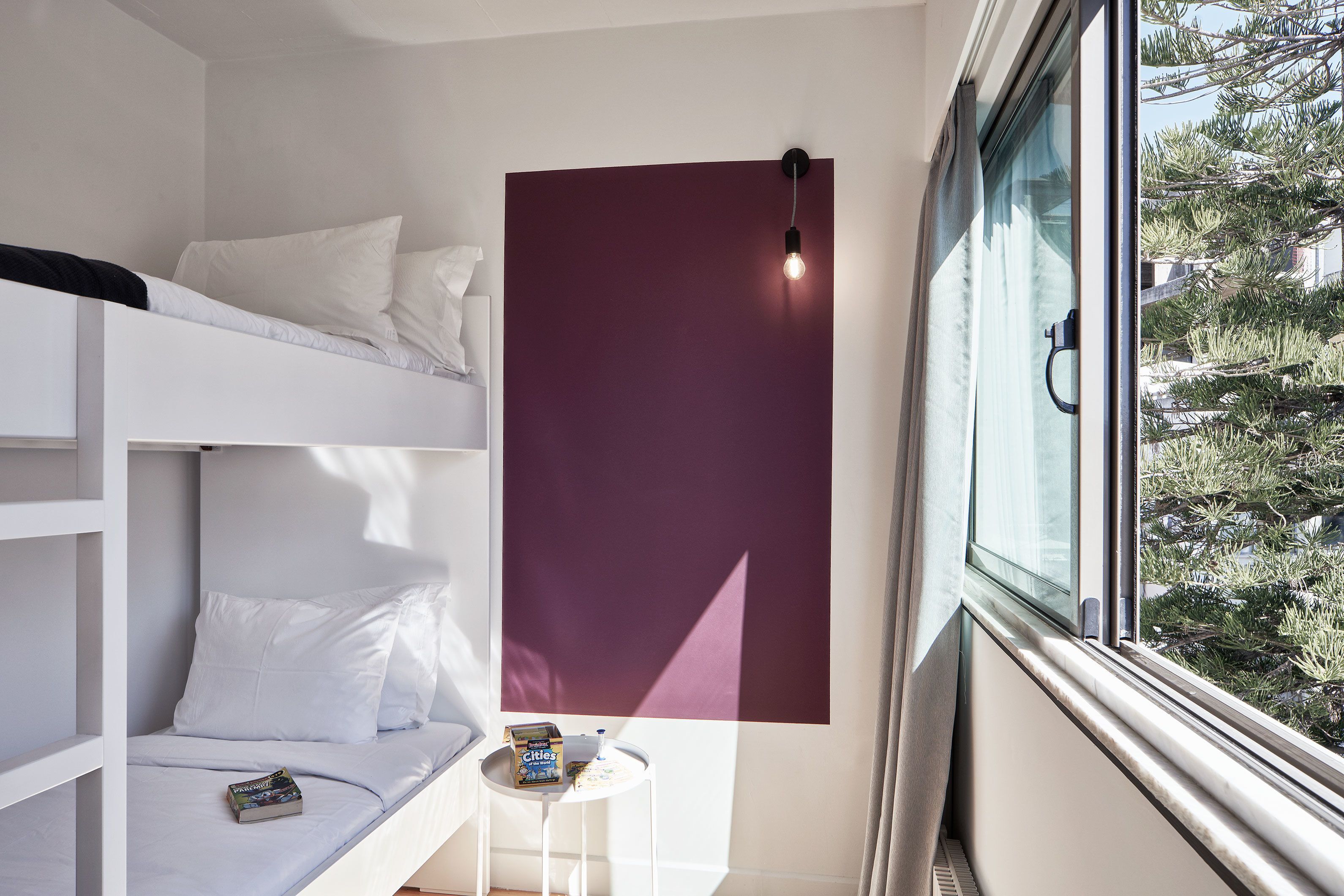 A room with a bunk bed, a small table with a box, and a window with a view of trees.