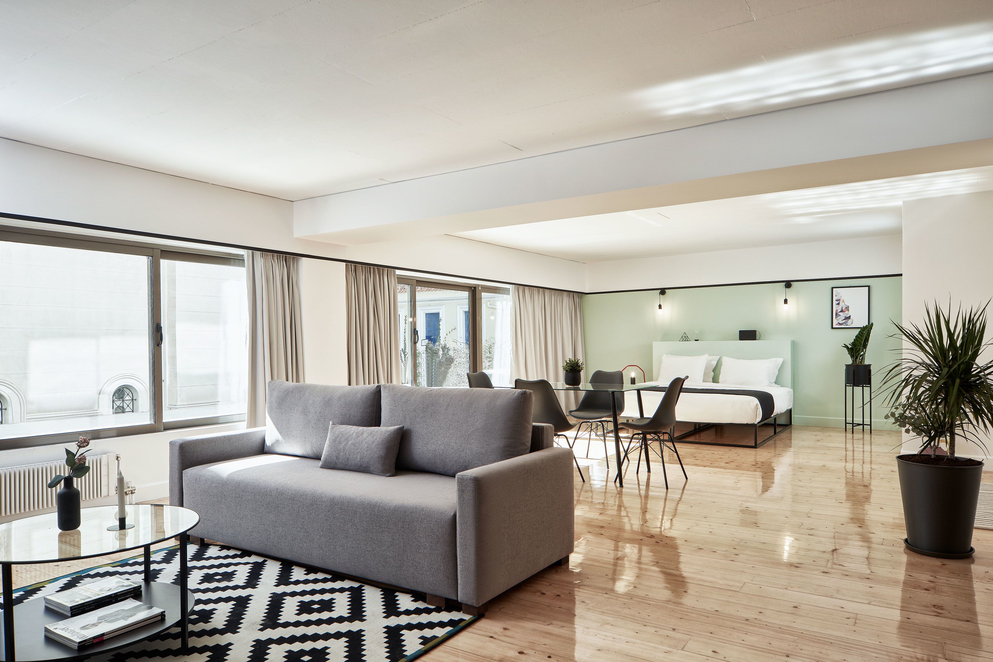 Ein modernes Wohnzimmer mit einem grauen Sofa, einem Glastisch und einem schwarz-weißen Teppich.