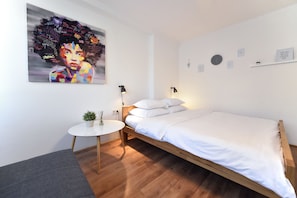 A modern bedroom with a wooden bed, a small round table with a plant, and a large abstract painting on the wall. - Vla Vla Apartments (Zagreb)
