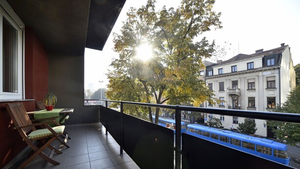 A balcony with a view of a blue tram, a potted plant, and a table with chairs. - Vla Vla Apartments (Zagreb)