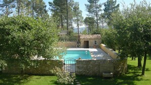 Un área de piscina privada con pared de piedra, un pequeño edificio y vistas despejadas a los árboles circundantes.