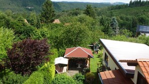Una casa con techo rojo y fachada blanca, rodeada de abundante vegetación y un paisaje boscoso.