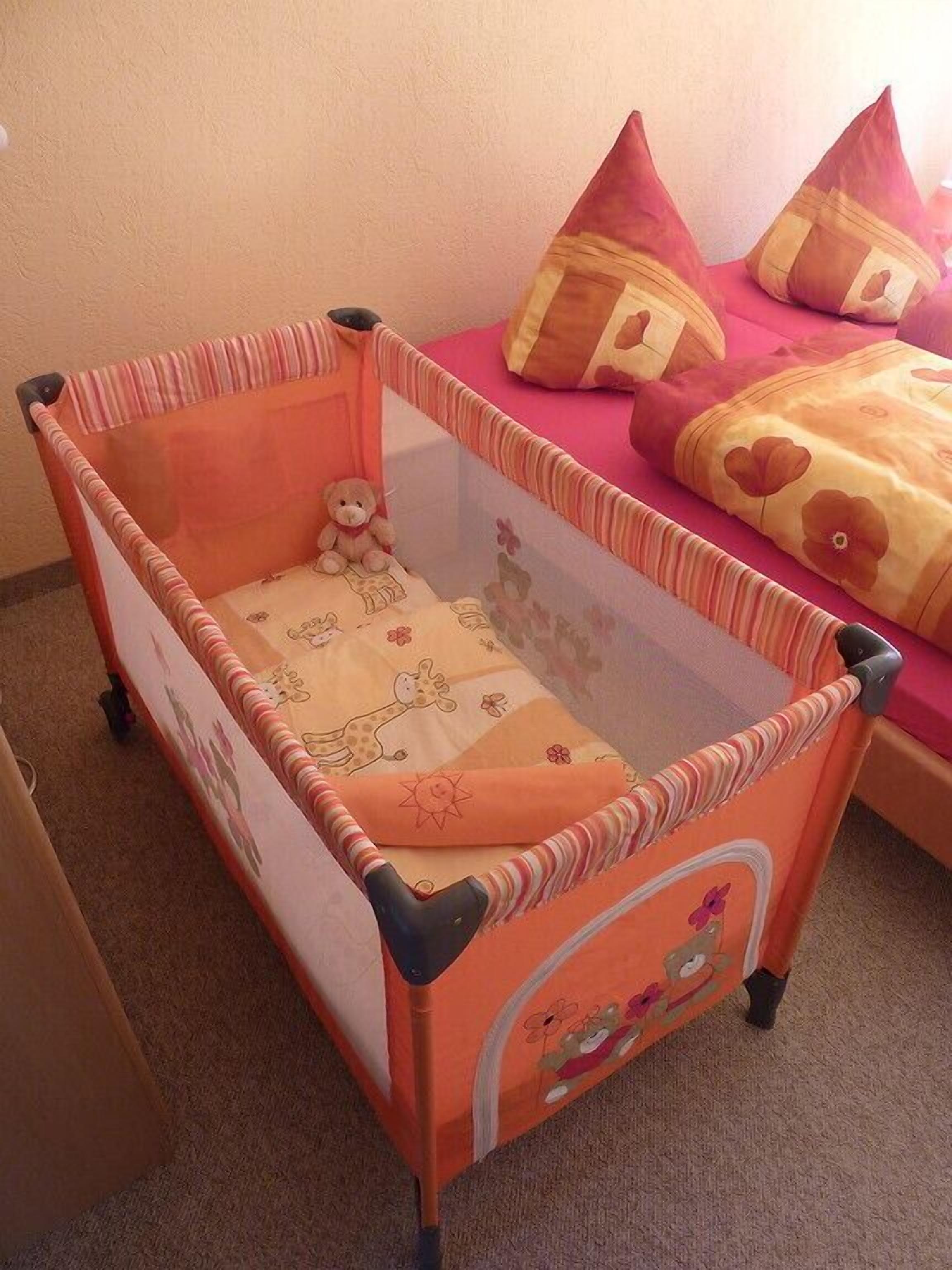 A baby crib with a giraffe-themed mattress and a teddy bear inside.