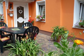 An outdoor patio with a table and chairs, surrounded by potted plants and flowers.