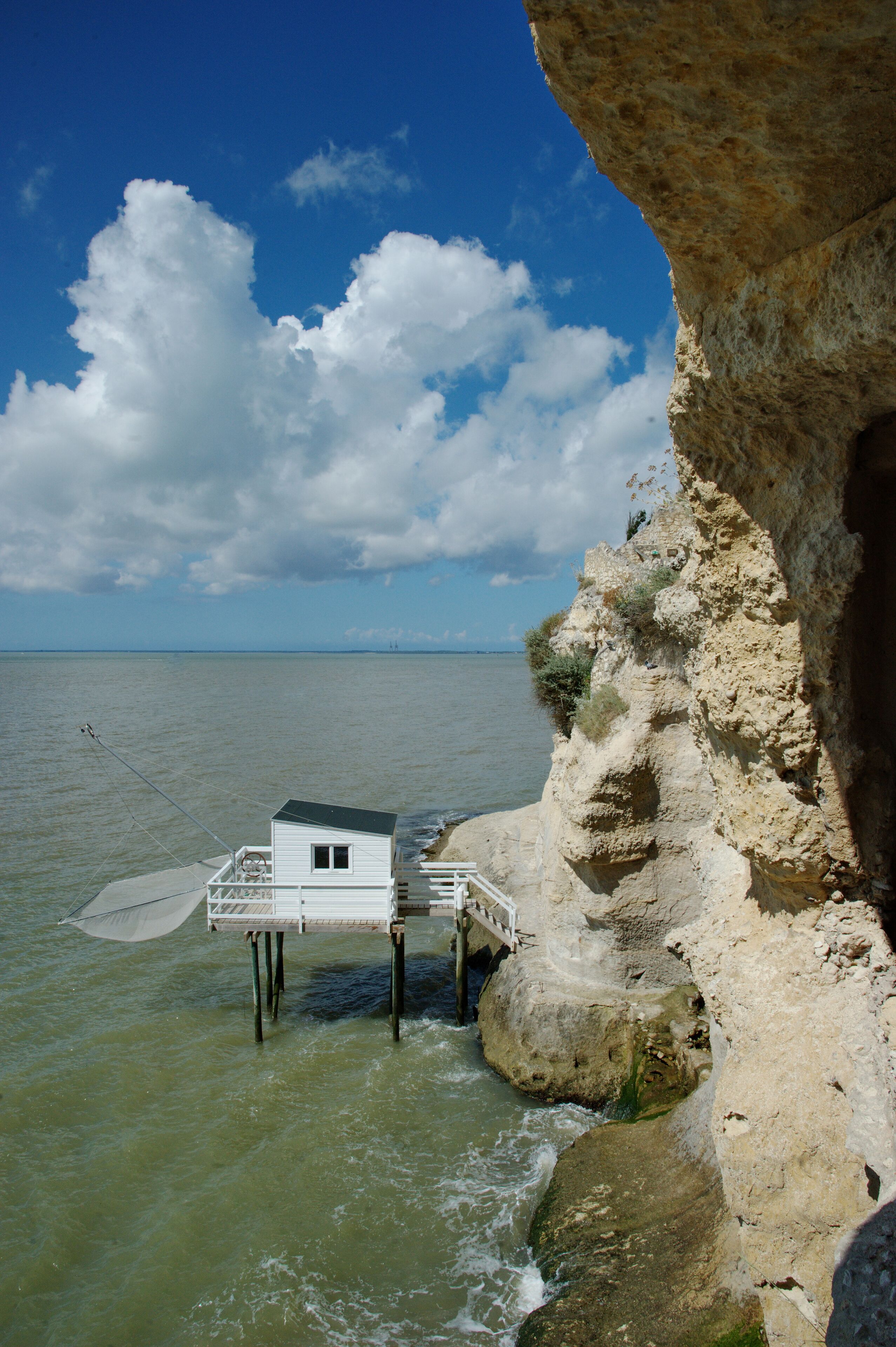 A white building with a balcony overlooking a rocky coastline and the sea.