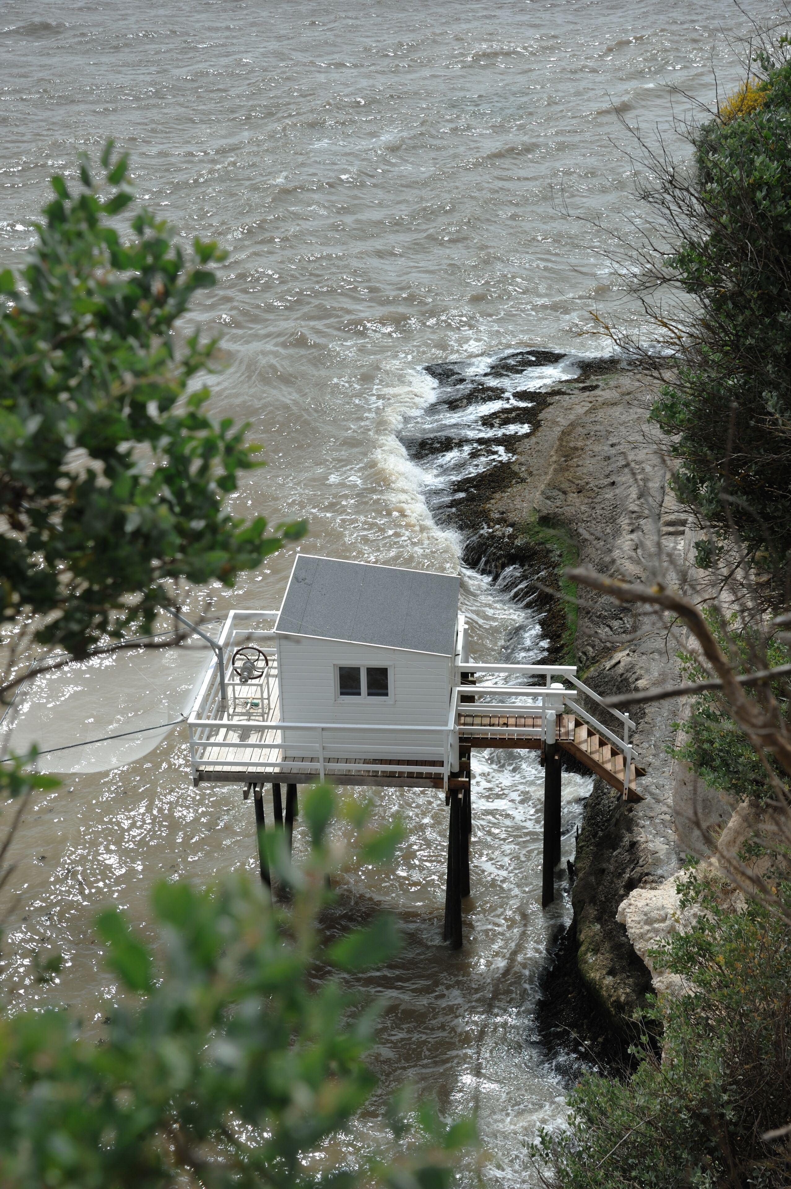 Ein Haus auf Stelzen über einem Fluss, mit einer Holzterrasse und einer kleinen Treppe, die zu ihm hinaufführt.