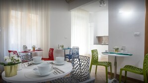 Un espace repas avec des tables et des chaises rondes, une cuisine à l’arrière-plan et une ambiance lumineuse et aérée.