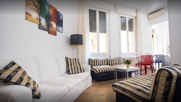 Un salon avec un canapé blanc, des fauteuils à rayures, une petite table et un fauteuil rouge.