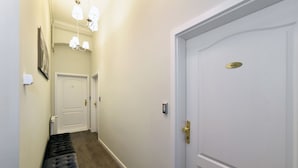 Un couloir étroit avec un banc, une porte portant une plaque avec un nom et un luminaire.
