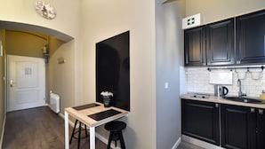 Une cuisine de taille réduite avec des meubles de couleur sombre, un plan de travail blanc et un tabouret noir.