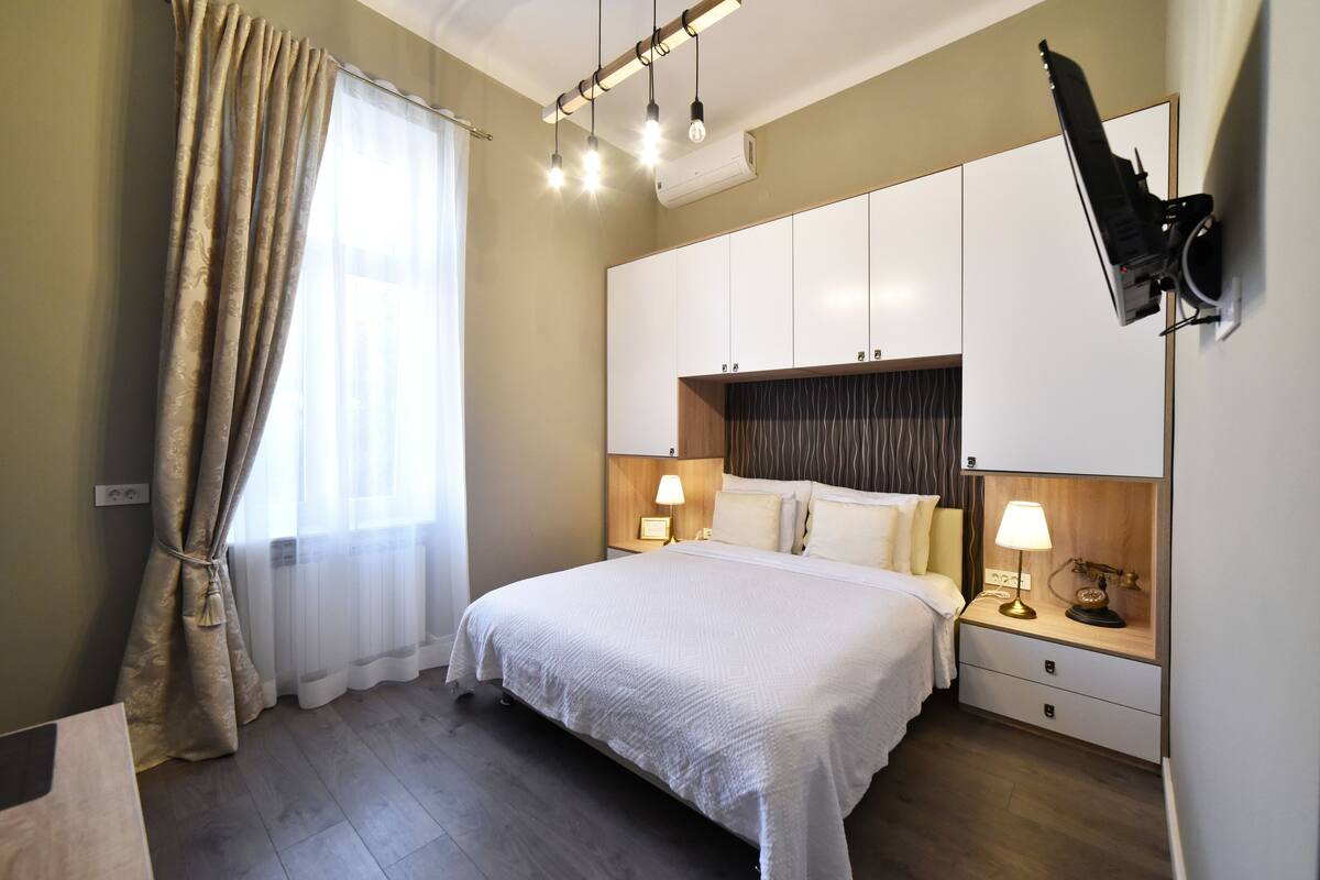 Ein Hotelzimmer mit einem großen Bett, Nachttischlampen, einem an der Wand montierten Fernseher und einem Holznachttisch.