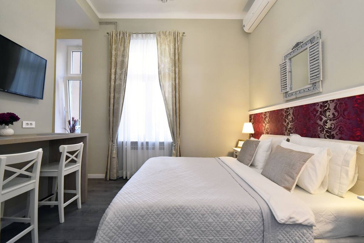 Ein Hotelzimmer mit einem Bett, einem Schreibtisch mit Stühlen, einem Fernseher und einem Fenster mit Vorhängen.