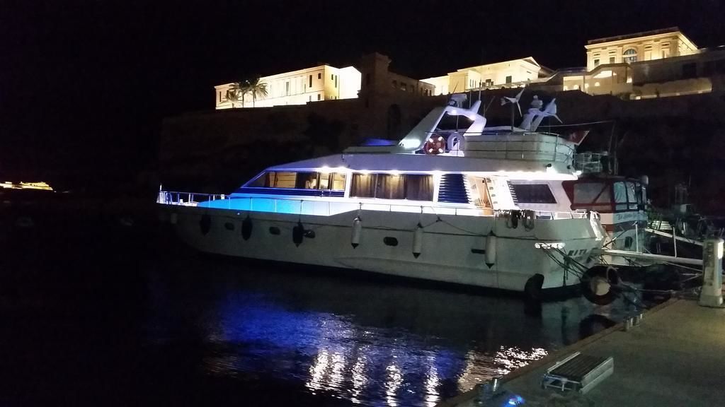 A large, well-lit yacht docked at a marina with a building in the background.