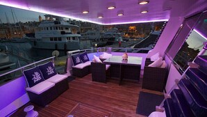 A deck with seating and a table, overlooking a marina with boats. - Riti Yacht (Kalkara)