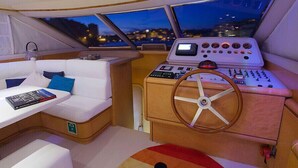 A boat's interior with a white cushioned seating area, a control panel with multiple gauges, and a steering wheel. - Riti Yacht (Kalkara)